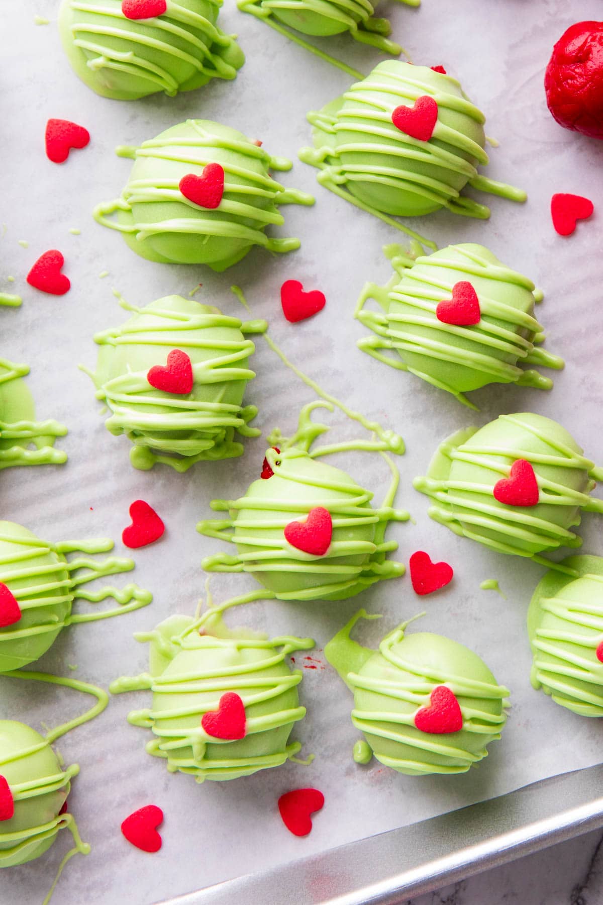 Grinch Oreo Balls on a lined sheet feature a chocolate candy coating around Oreo cookie crumb centers and a red heart sprinkle.