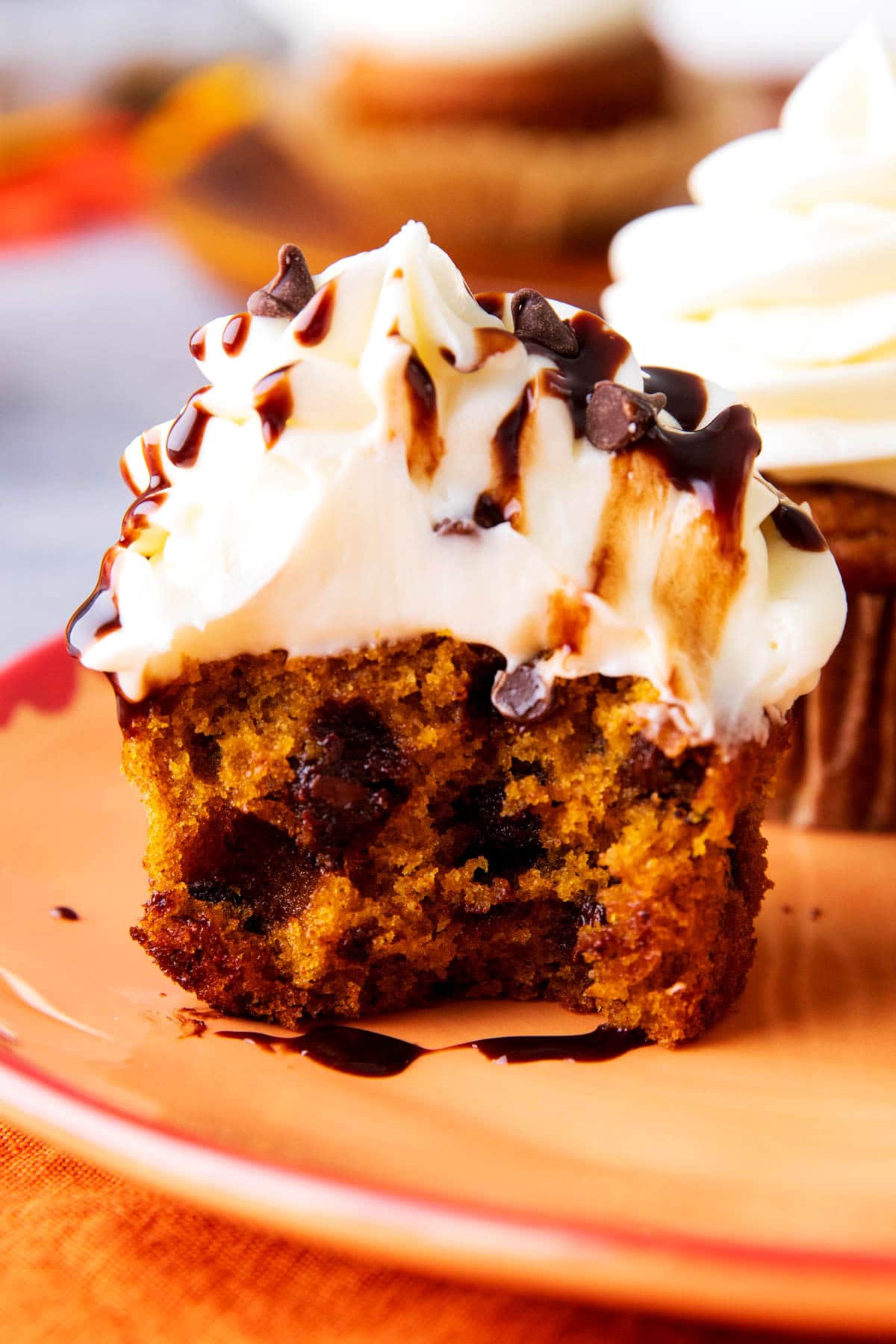 A pumpkin chocolate chip cupcake bitten in half on a fall dessert plate.