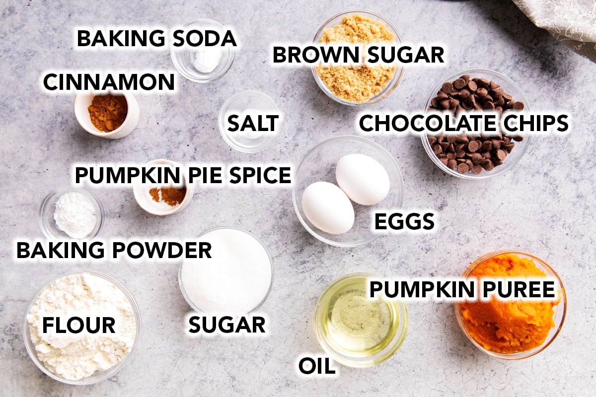 Pumpkin chocolate chip cupcakes recipe ingredients in prep bowls - flour, butter, eggs, pumpkin puree, chocolate chips, baking powder, baking soda, pumpkin pie spice, cinnamon, and brown sugar.