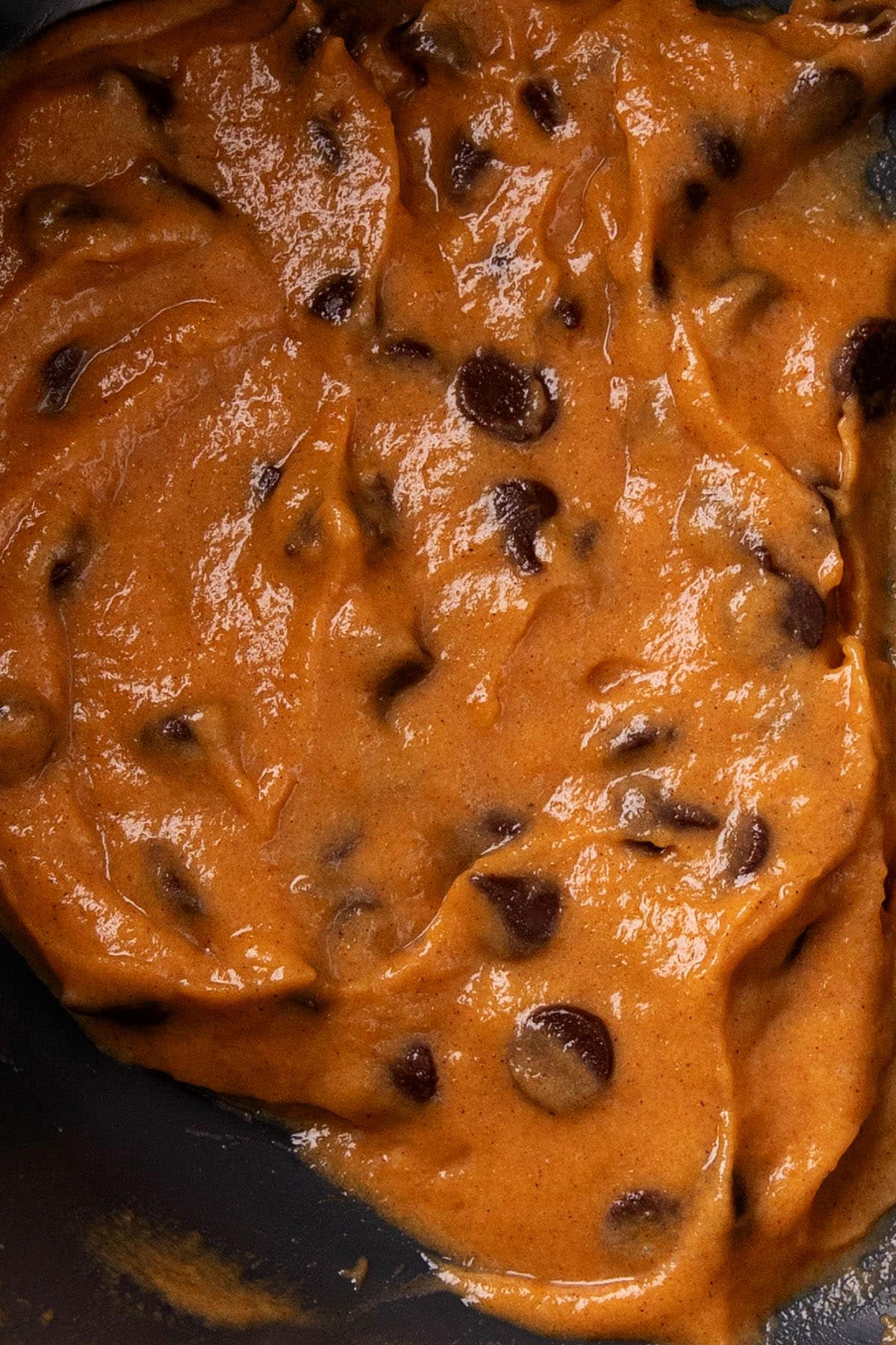 Pumpkin chocolate chip cupcakes batter in a mixing bowl with lots of pumpkin puree and loads of chocolate chips.