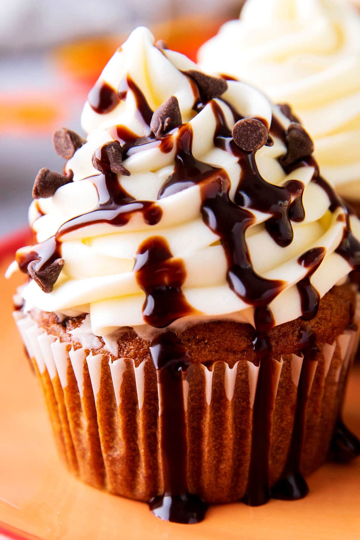 Close up of pumpkin chocolate chip cupcakes topped with cream cheese frosting, mini chocolate chips, and chocolate drizzle.