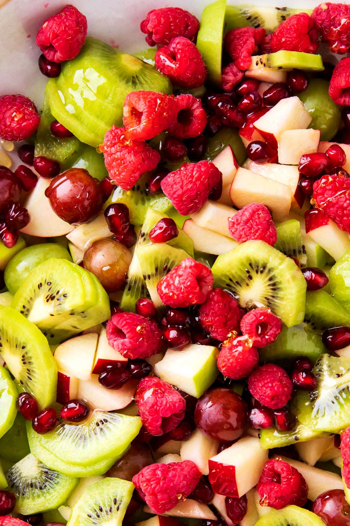 Close up of easy Christmas fruit salad with juicy kiwis fruit, raspberries, red and green apples, and pomegranate shows the festive holiday colors in this recipe.