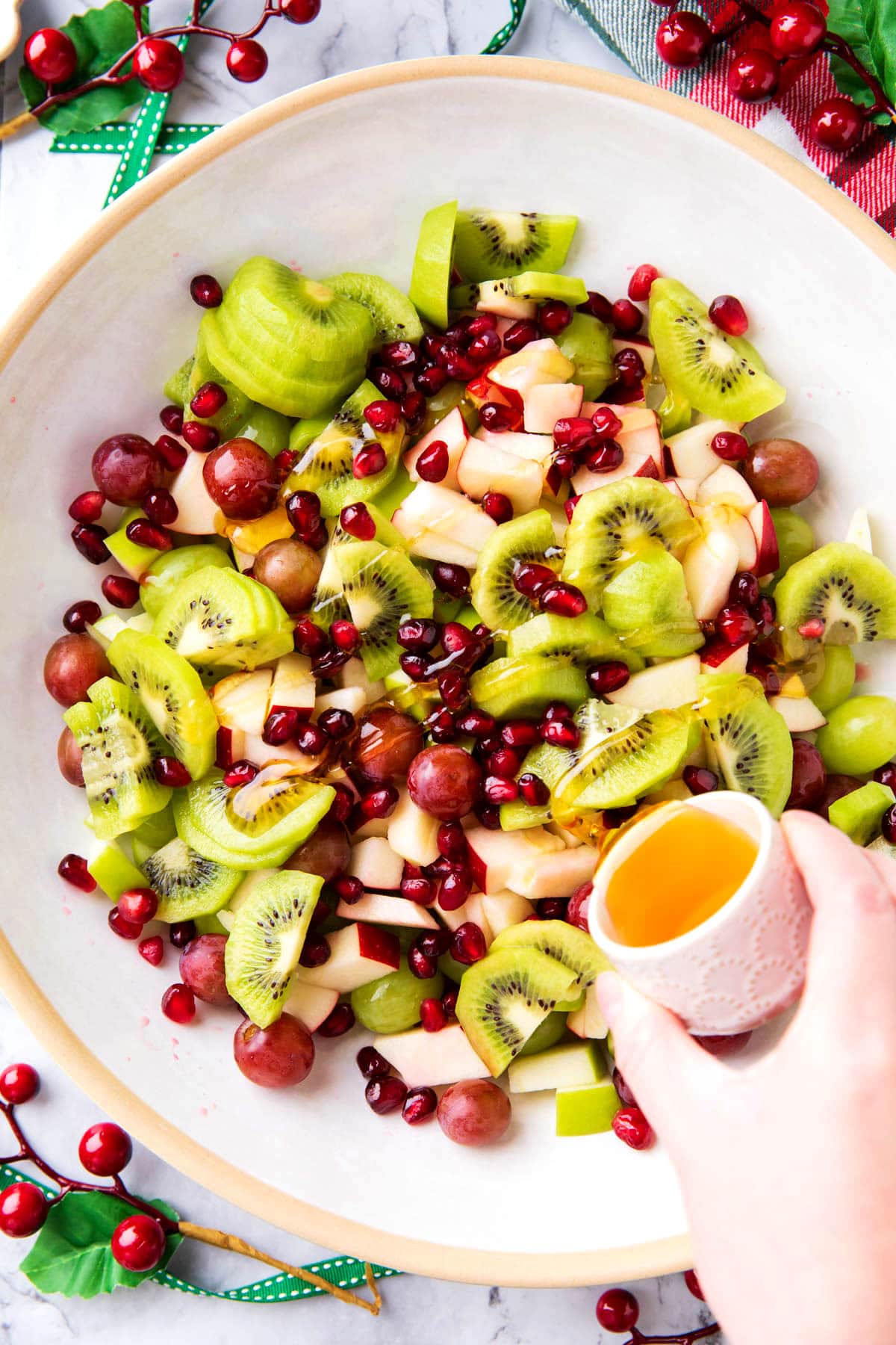 Pouring honey lime dressing over Christmas holiday fruit salad recipe.