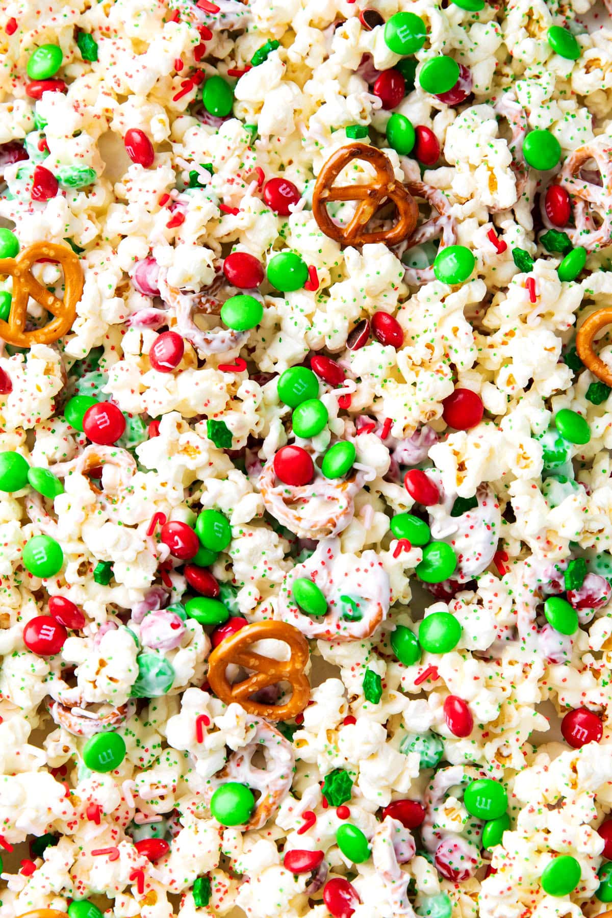 Christmas crunch spread out on a lined baking sheet packed with candy, Christmas sprinkles, and popcorn for a holiday-ready treat also called white chocolate popcorn.