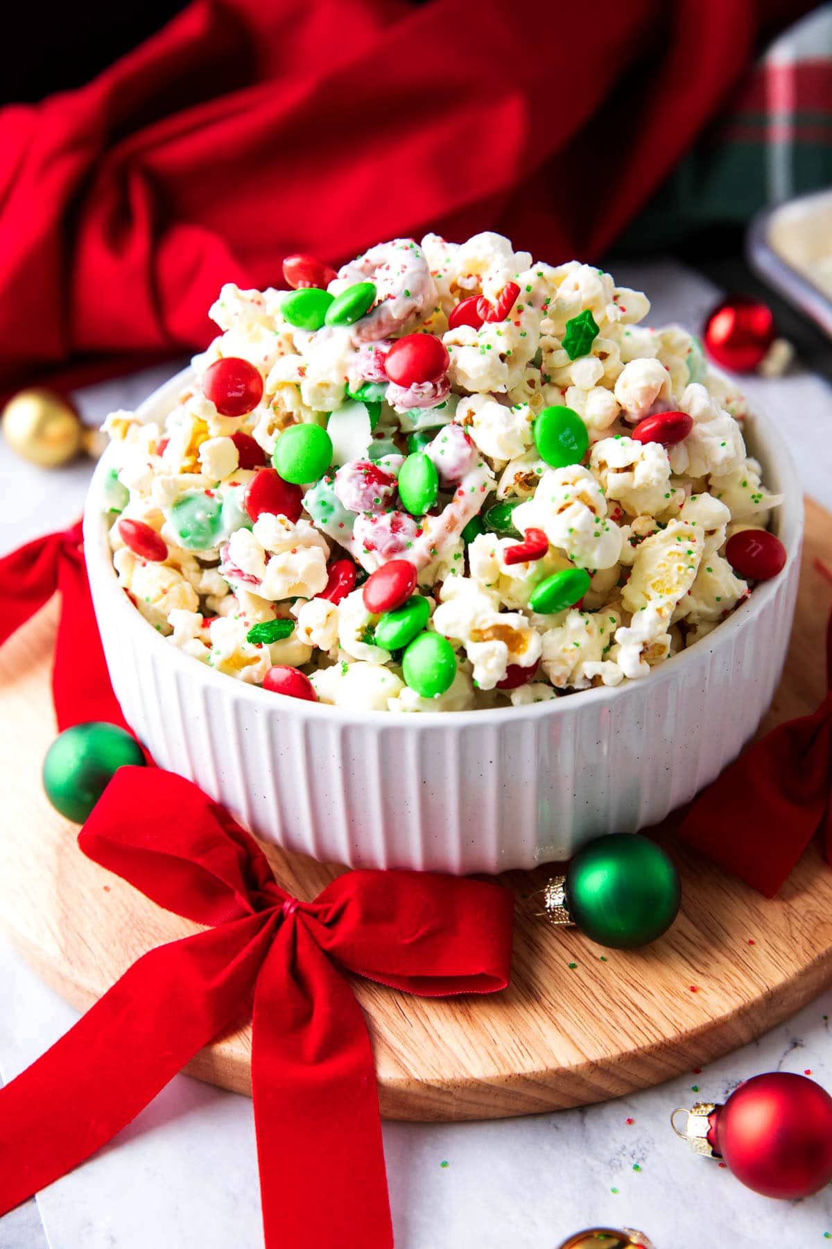 This Christmas popcorn recipe is coated in white chocolate and served in a bowl with red ribbons, green ornaments, and more festive Christmas decor.