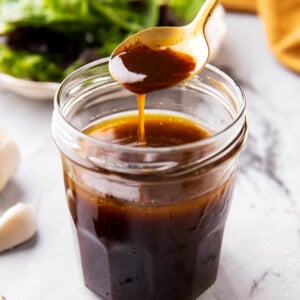 Someone scooping a spoon of balsamic vinaigrette dressing out of of a salad dressing jar