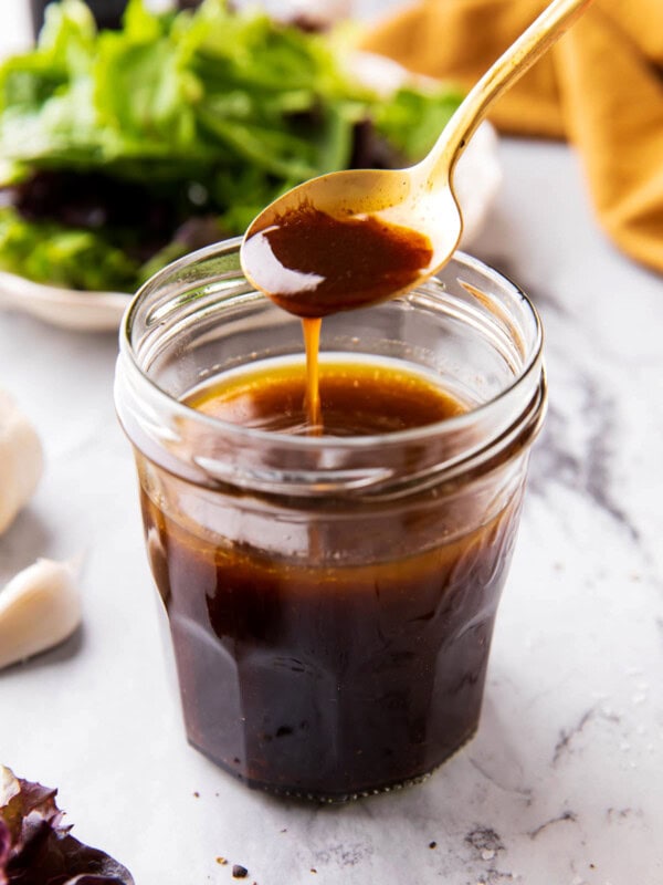 Someone scooping a spoon of balsamic vinaigrette dressing out of of a salad dressing jar