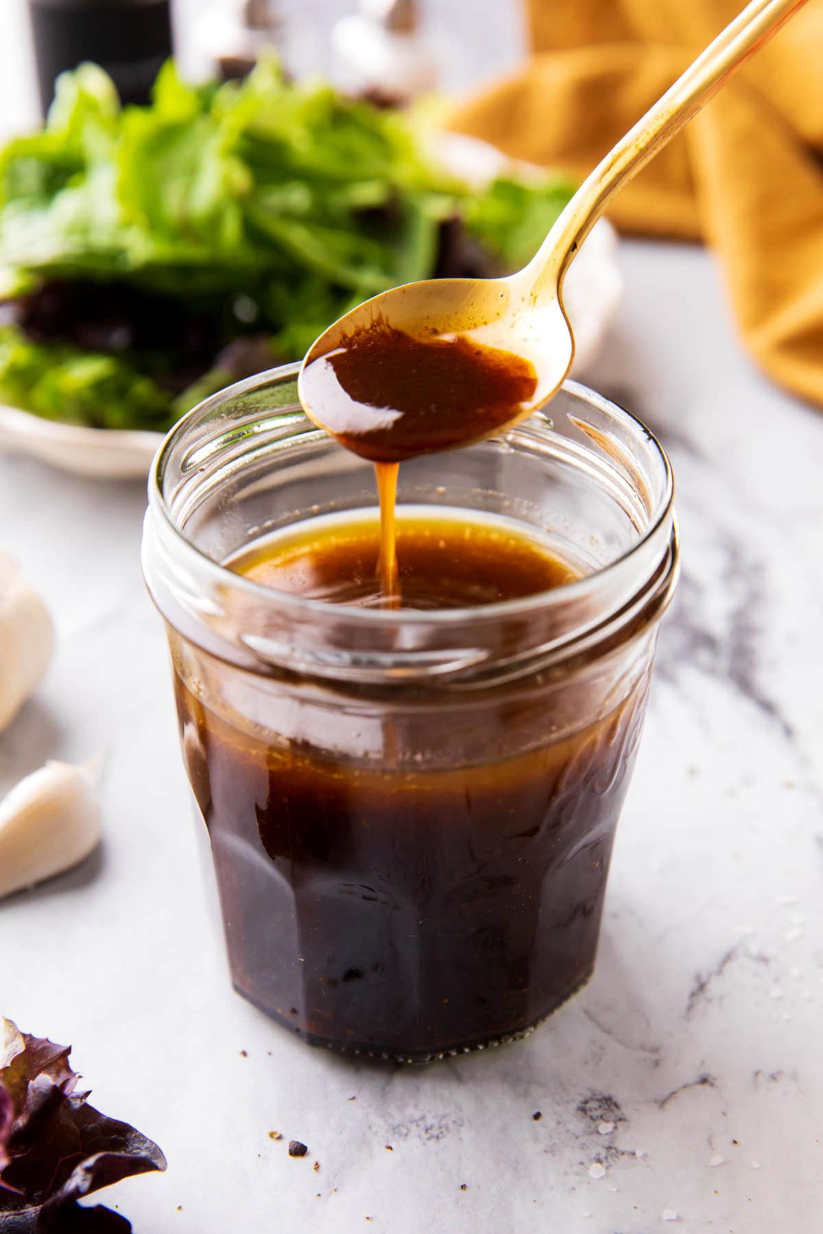 Someone scooping a spoon of balsamic vinaigrette dressing out of of a salad dressing jar.