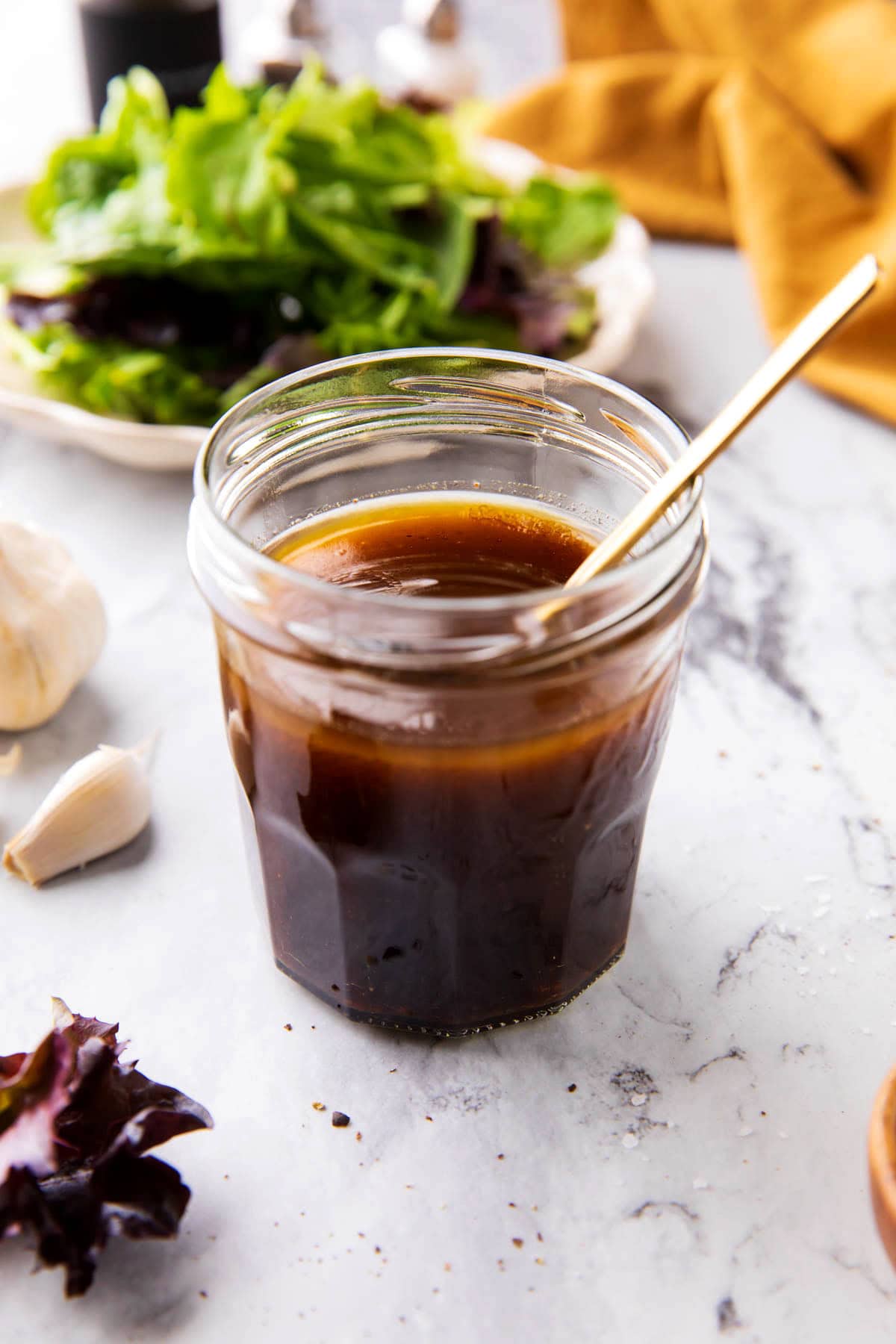 Balsamic dressing that is tangy and sweet, perfect for drizzling over salad, chicken, fish, and bread served in a salad dressing jar with leafy greens.