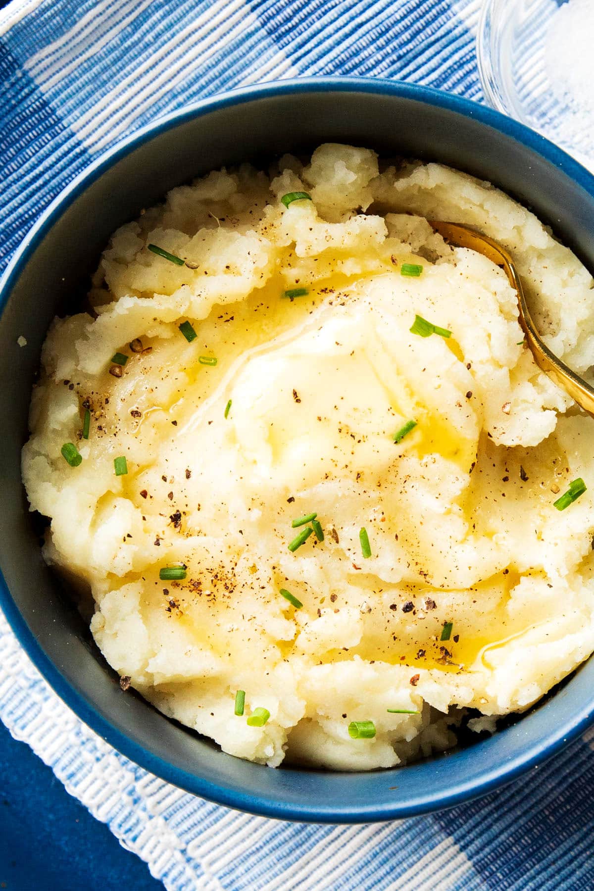 Quick and easy creamy mashed potatoes are served in a bowl topped with melted butter, chives, salt and pepper.