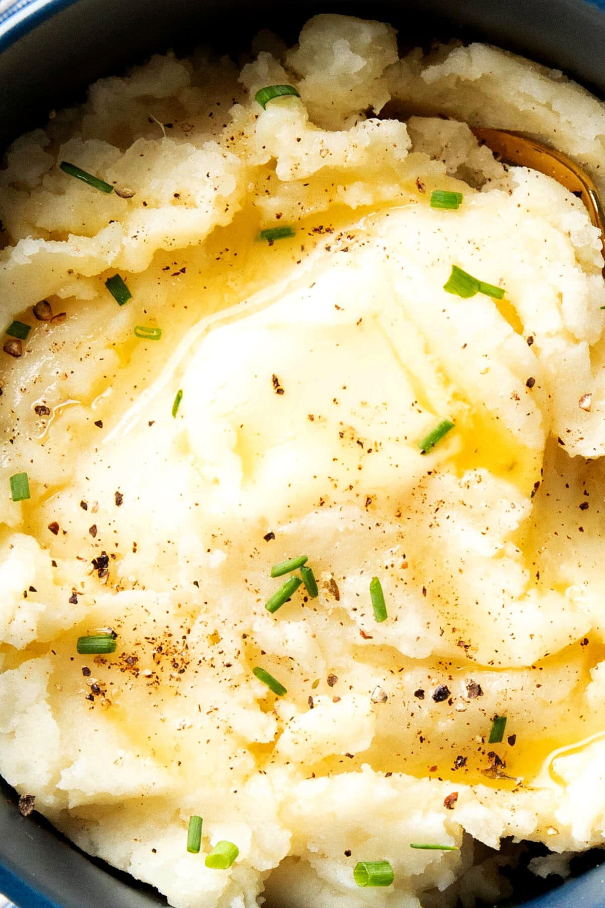 Close up of easy mashed potatoes recipe to show creamy and smooth texture topped with butter and chives.