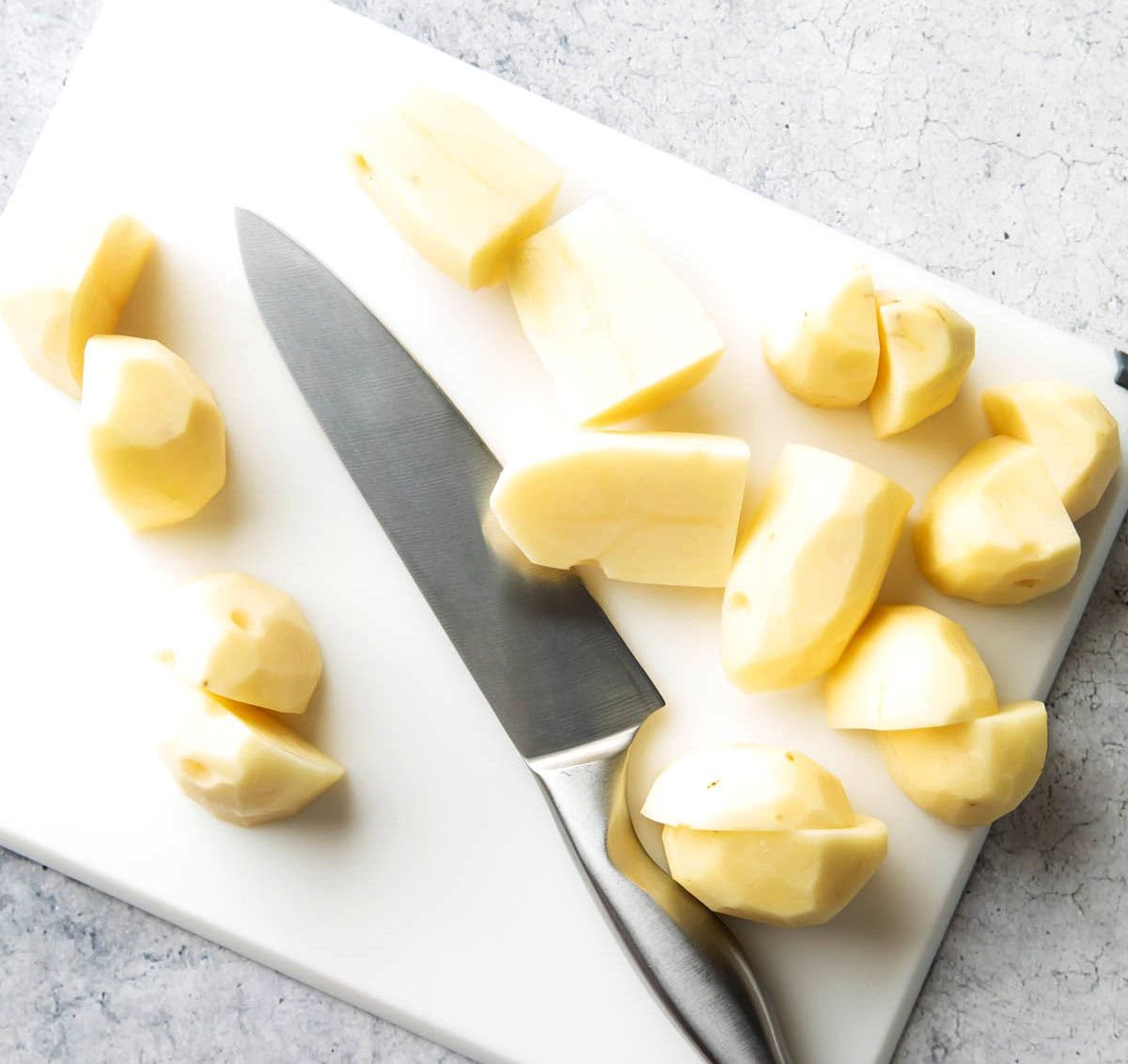A photo showing How to Make Mashed Potatoes - peeled and quartering potatoes with a knife.