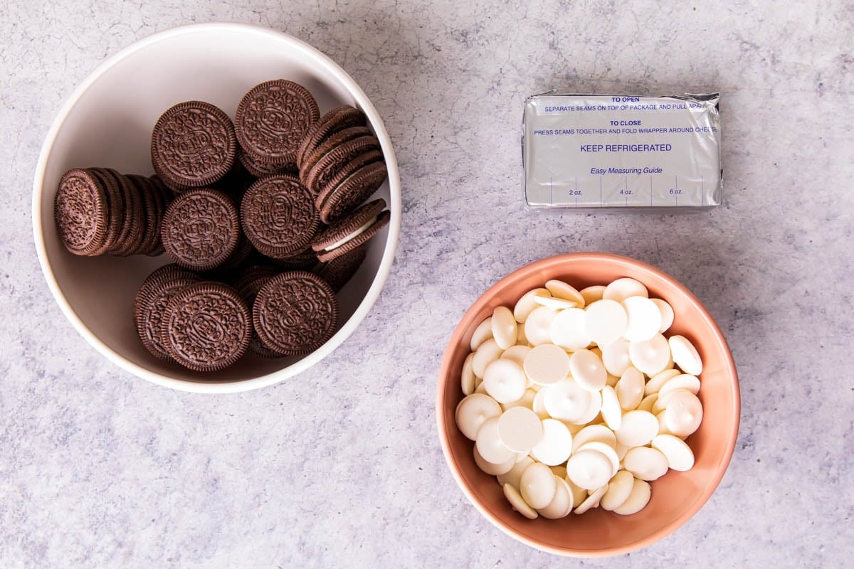 Showing Oreo truffles 3 ingredients on a table including Oreo cookies, white chocolate candy melts, and cream cheese.