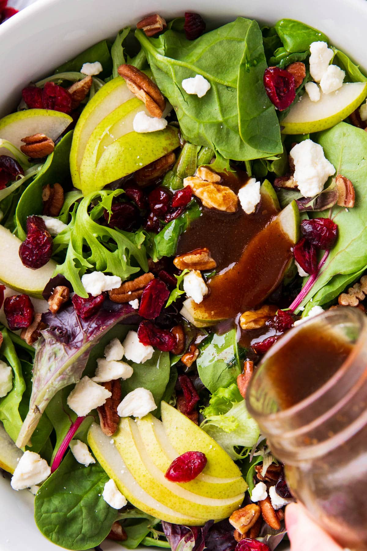 Close up of someone pouring balsamic vinaigrette over Pear Salad with juicy pears, cranberries, nuts, and gorgonzola cheese.