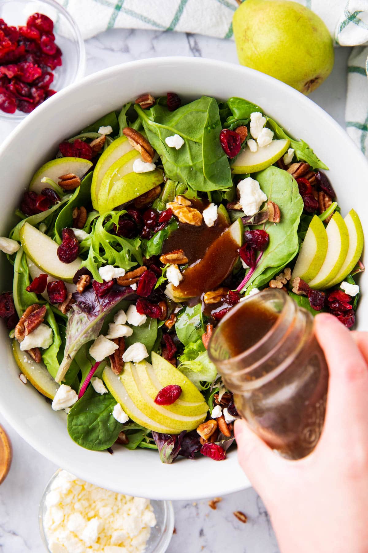 Pouring balsamic dressing over Pear Salad. This balsamic vinaigrette is a deep brown with tangy and lightly sweet flavor.