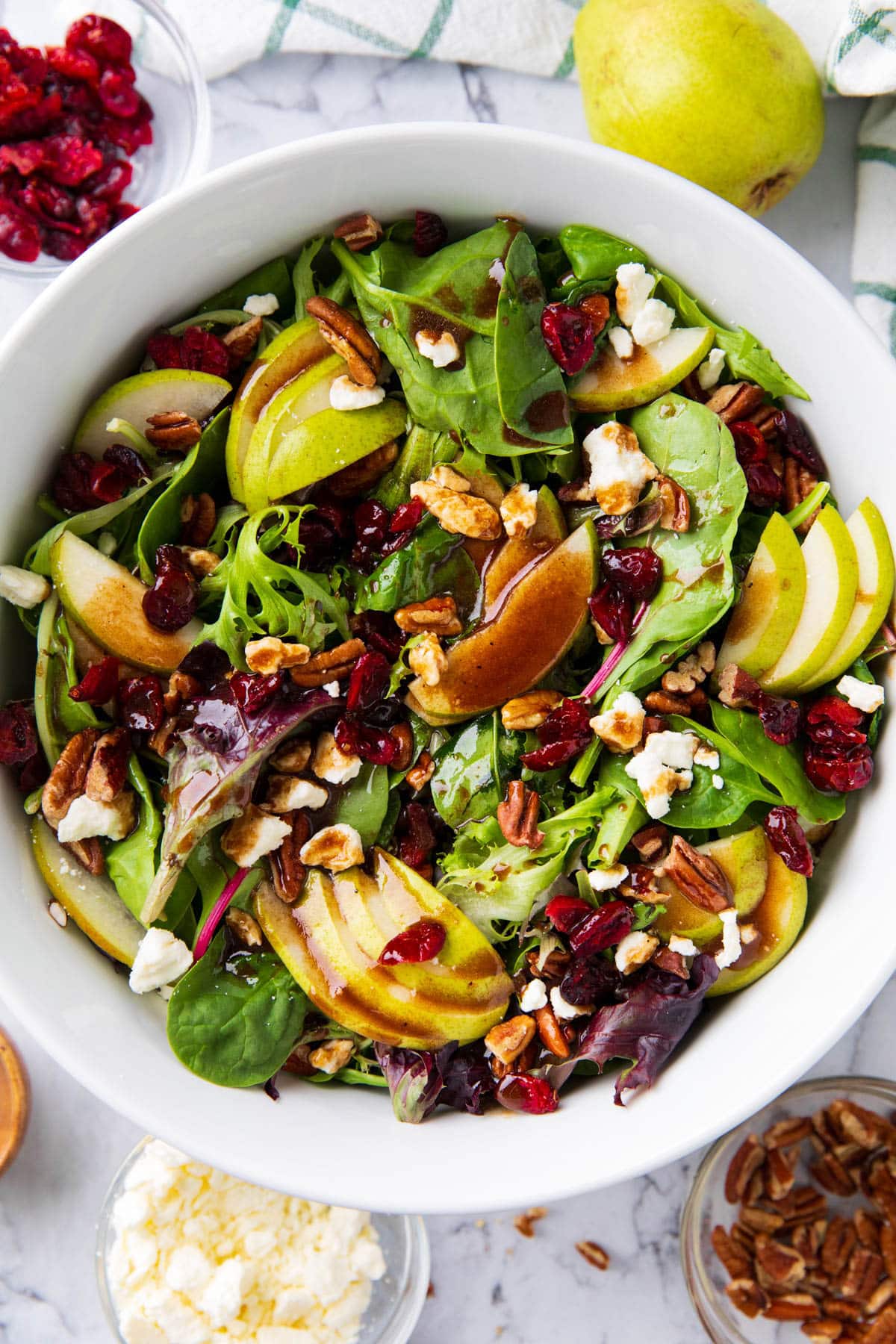 Pear salad served in a salad bowl with pears, dried cranberries, and feta cheese on a dining table.