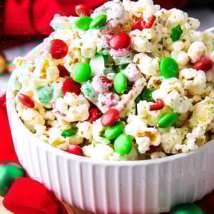 This delicious Christmas Popcorn Recipe served in a festive bowl packed with salty popcorn, pretzels, red and green M&M's and drizzled with white chocolate