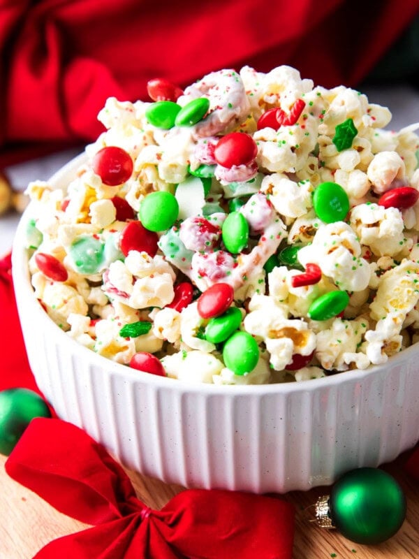 This delicious Christmas Popcorn Recipe served in a festive bowl packed with salty popcorn, pretzels, red and green M&M's and drizzled with white chocolate