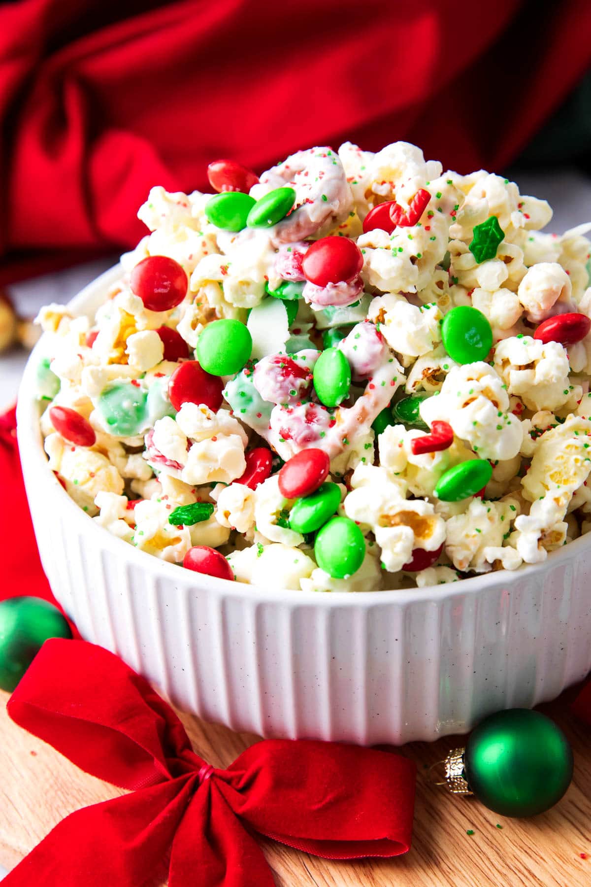 This delicious Christmas Popcorn Recipe served in a festive bowl packed with salty popcorn, pretzels, red and green M&M's and drizzled with white chocolate.
