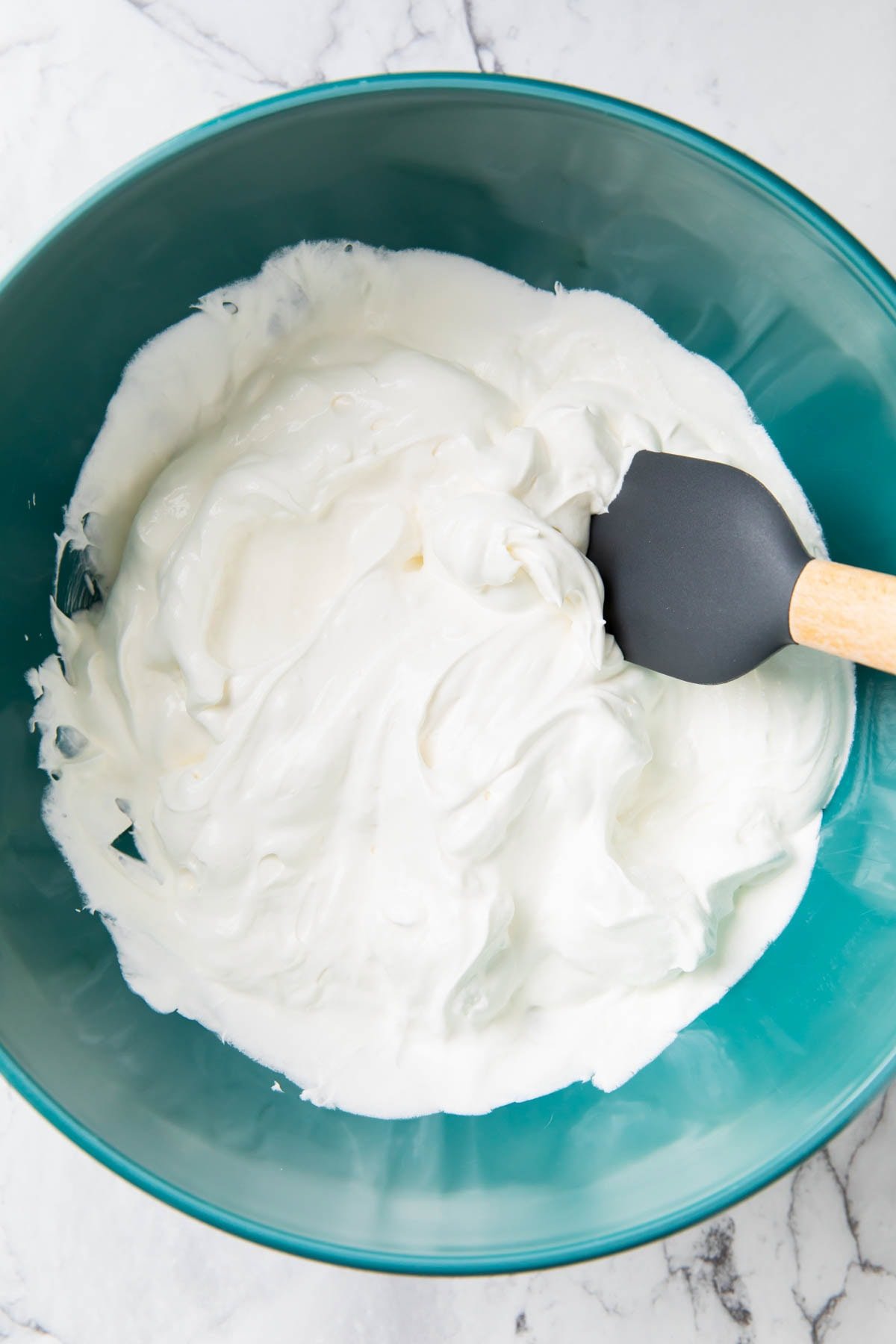 A photo showing how to make Ambrosia Salad - Folding Cool Whip frozen whipped topping and vanilla yogurt together to make creamy fruit salad dressing.