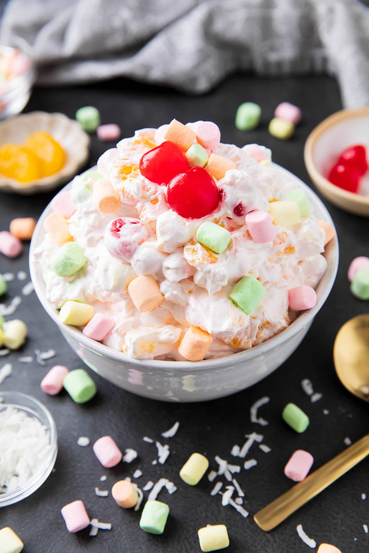 Ambrosia watergate salad is served with lots of marshmallows, topped with maraschino cherries, and extra fruit topping.