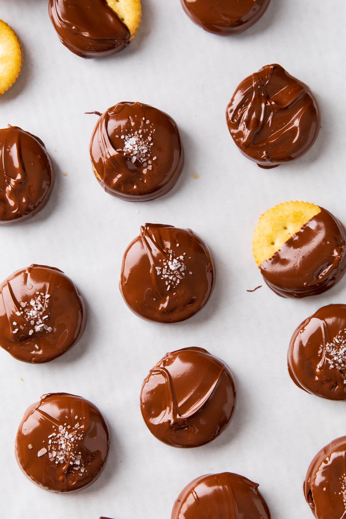 Peanut butter chocolate ritz cookies are chocolate covered on a parchment lined baking sheet for the chocolate to set.