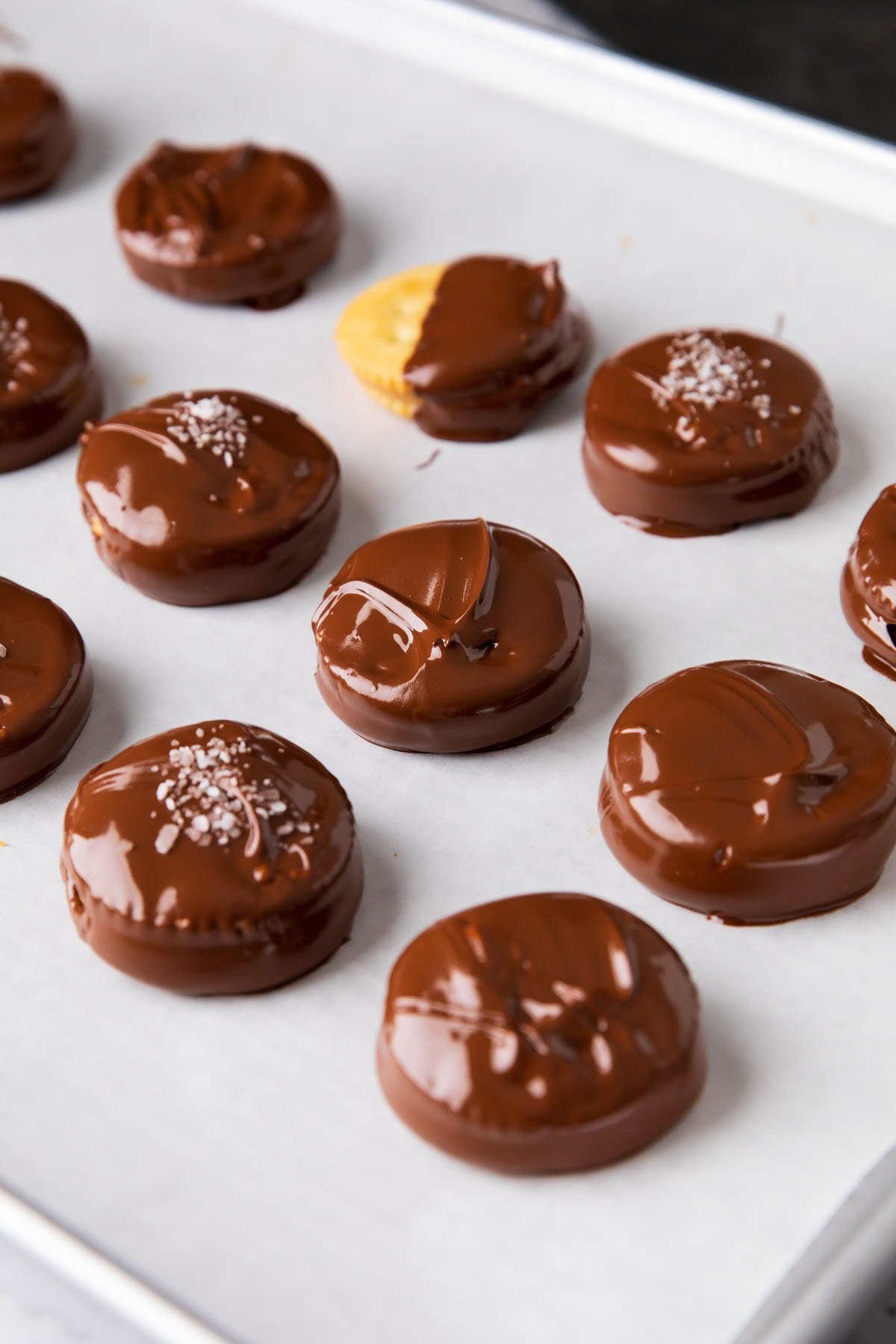 Neatly lined up chocolate peanut butter Ritz cookies are dipped in chocolate on a lined sheet.