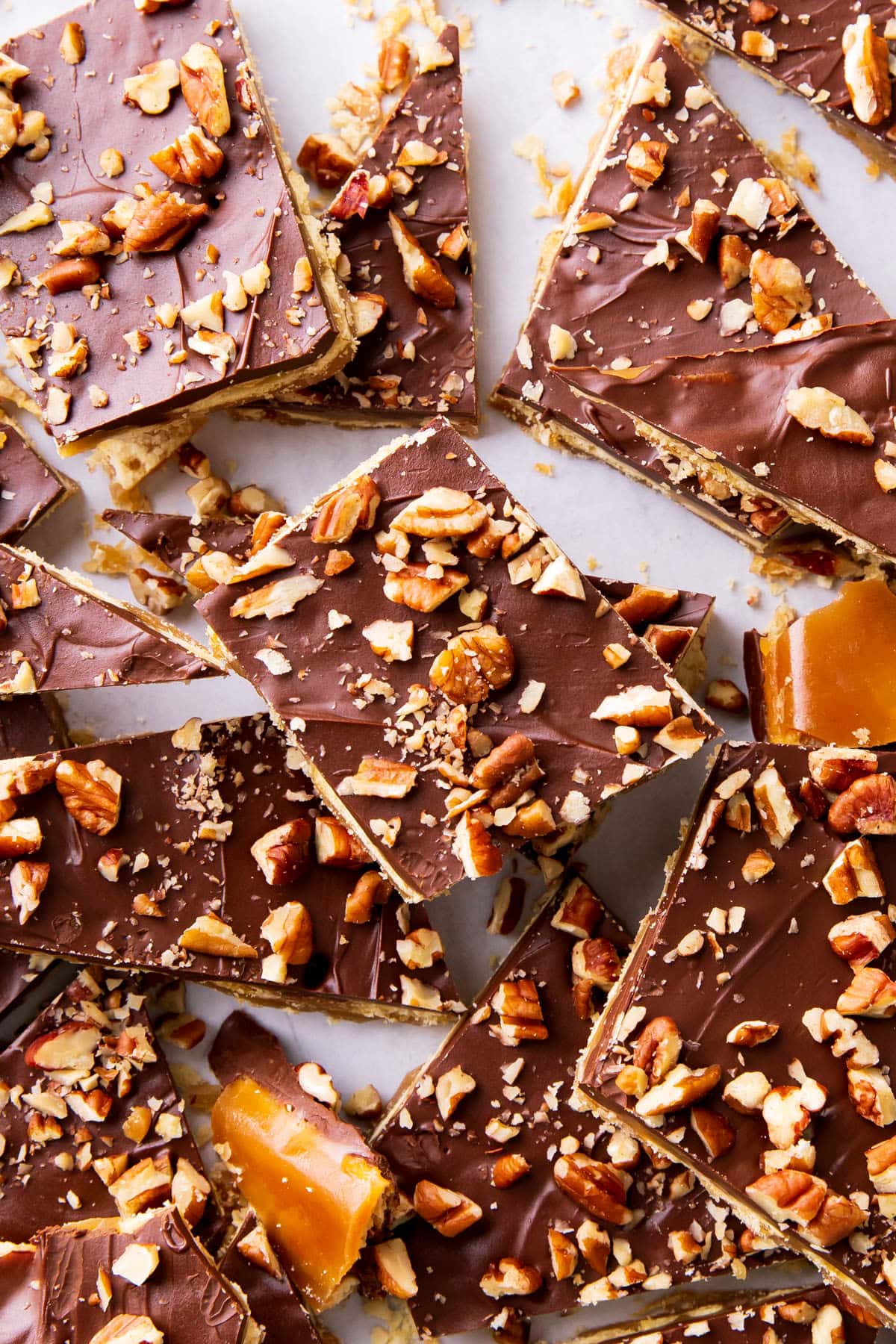 Saltine cracker toffee with toffee covered saltine crackers topped with chocolate and pecans, sliced into pieces on a sheet.