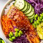 1 This easy salmon rice bowl recipe includes glazed salmon served over a bowl of rice, cabbage, cucumber, edamame, avocado and sesame seeds