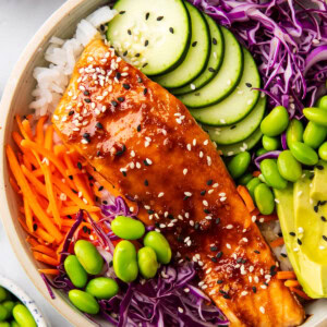 1 This easy salmon rice bowl recipe includes glazed salmon served over a bowl of rice, cabbage, cucumber, edamame, avocado and sesame seeds