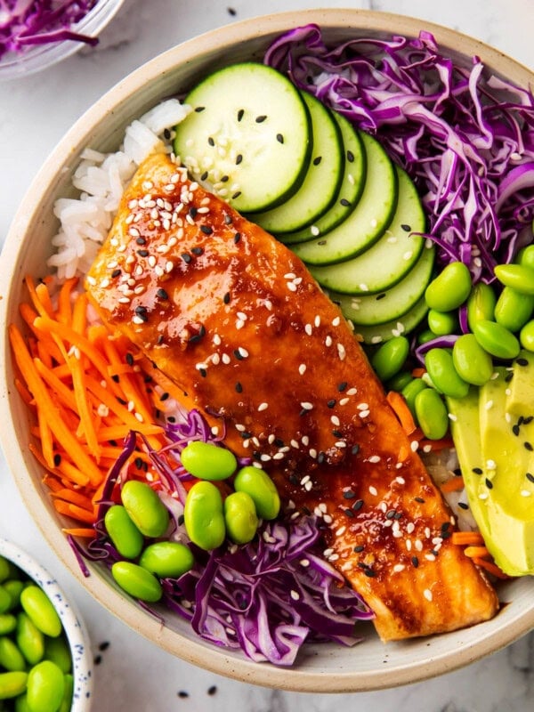 1 This easy salmon rice bowl recipe includes glazed salmon served over a bowl of rice, cabbage, cucumber, edamame, avocado and sesame seeds