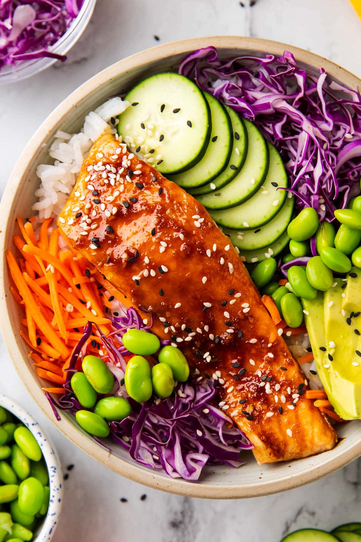 This easy salmon rice bowl recipe includes glazed salmon served over a bowl of rice, cabbage, cucumber, edamame, avocado and sesame seeds.