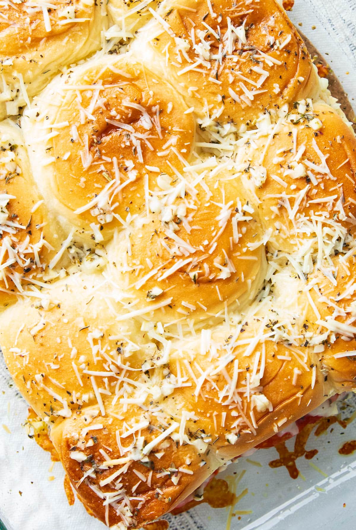 Close up of easy pizza sliders on Hawaiian rolls with lots of Italian seasoning and herbs.