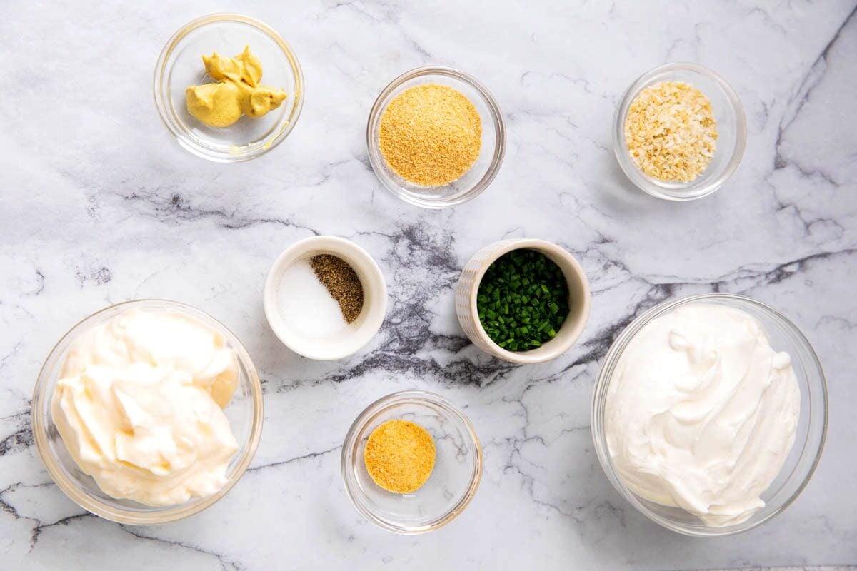 Sour cream and onion dip ingredients in prep bowls - sour cream, mayonnaise, minced onion, onion powder, Dijon mustard, garlic powder, salt, pepper, and chives.