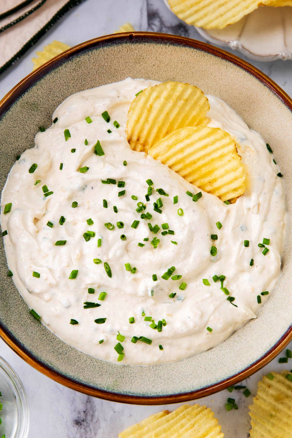 Sour cream and onion dip is served in a bowl topped with chives and garnished with potato chips.