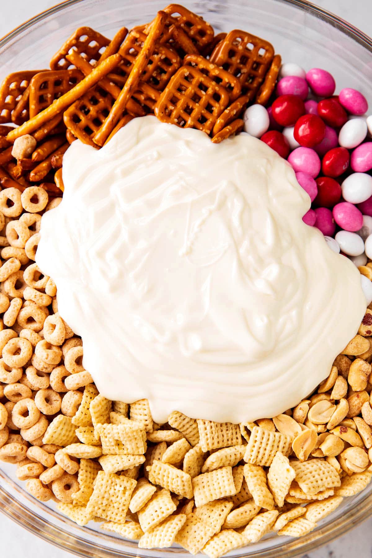 Close up of melted white chocolate on top of Valentine's Chex mix in a large mixing bowl.