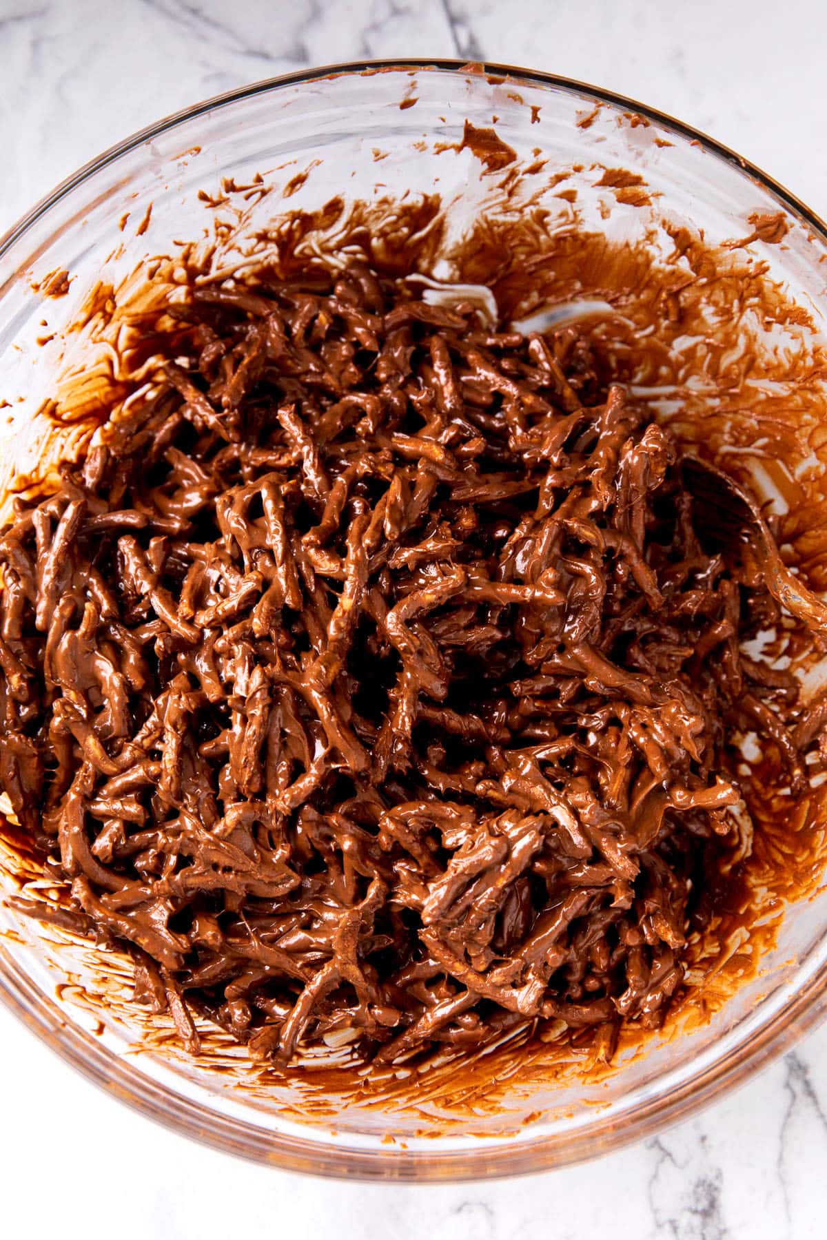 A photo showing How to Make Birds Nest Cookies - melted chocolate and peanut butter chips coat crunchy chow mein noodles in a mixing bowl.