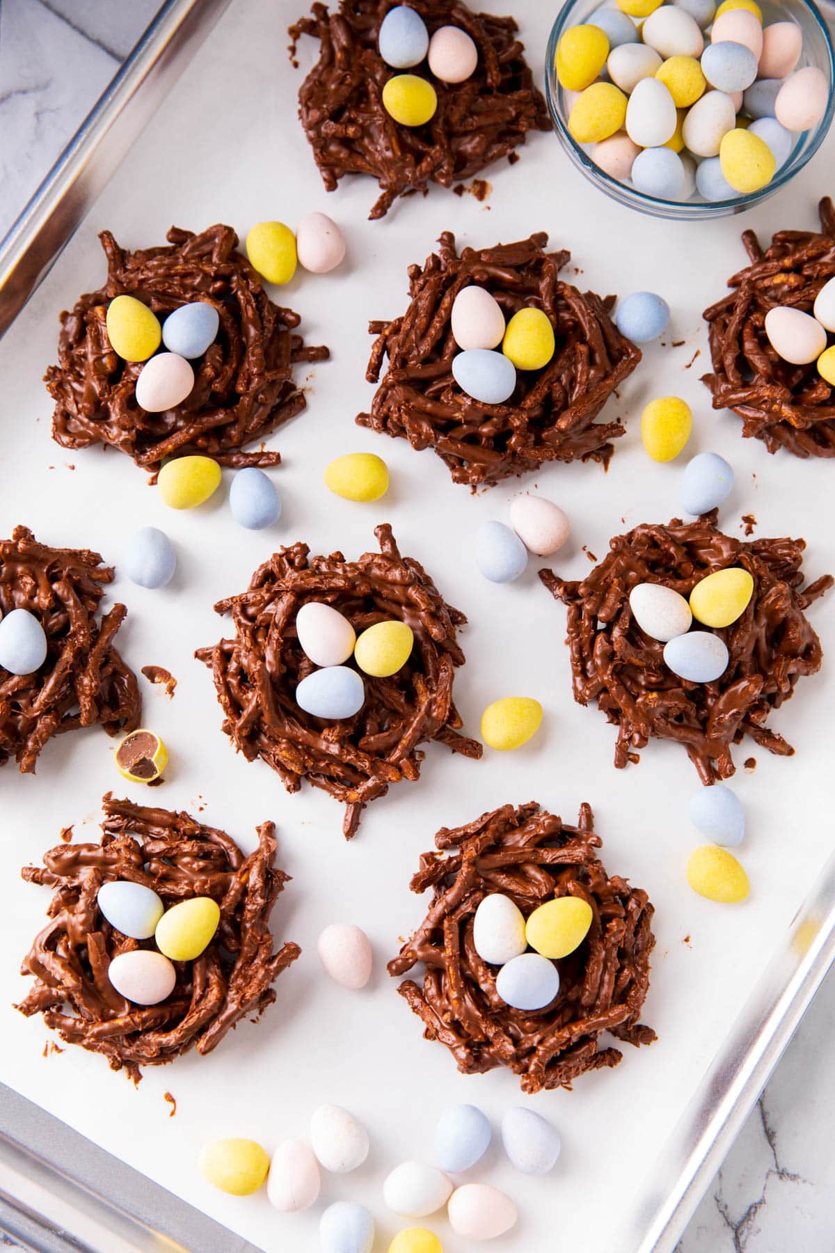 This no bake birds nest cookie recipe is shown with pastel colored chocolate mini eggs and more Easter recipe decorations.