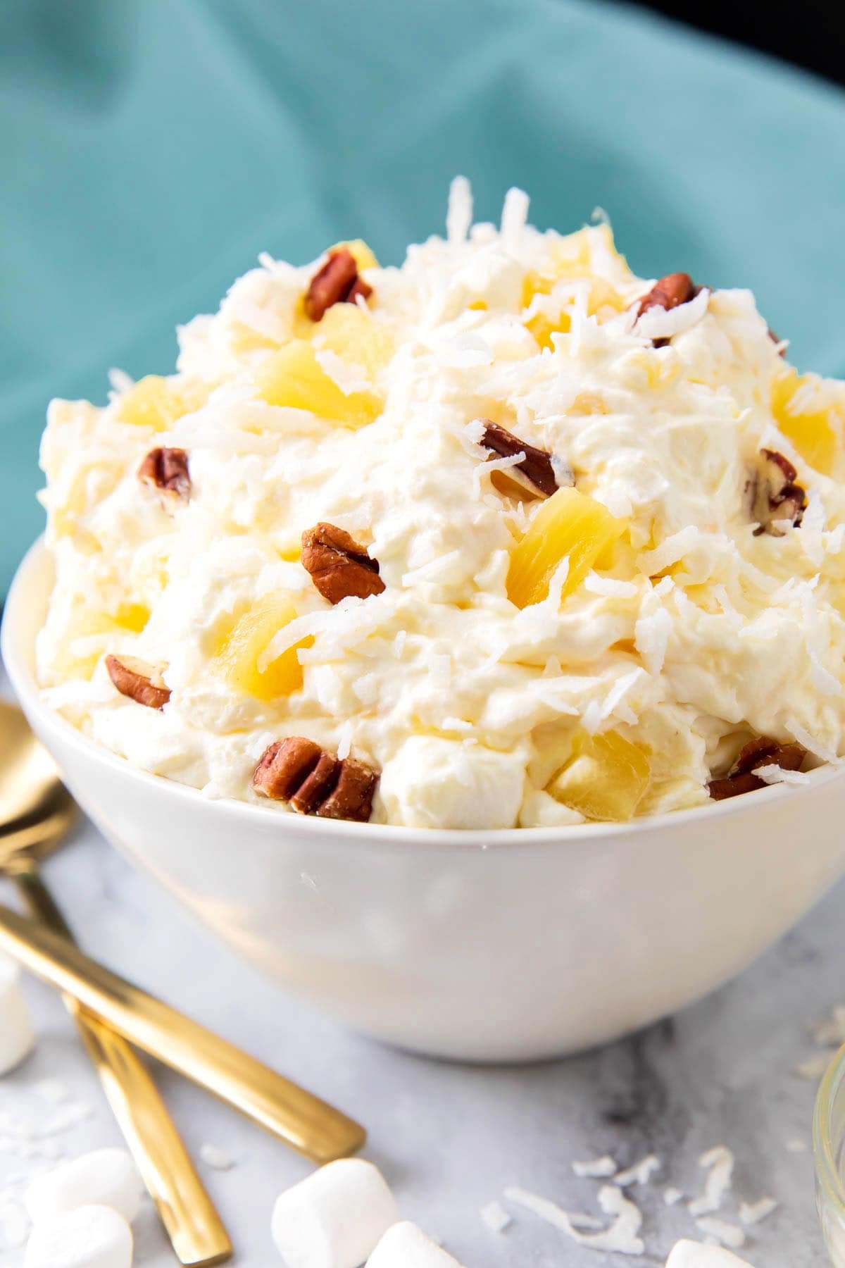 Close up of Pineapple Fluff recipe shows fluffy dessert packed with coconut, old fashioned pineapple and nuts.