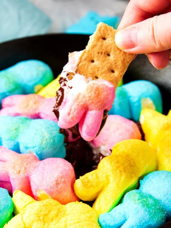 Someone dip a graham cracker into Easter Dip made with Peeps marshmallows and chocolate