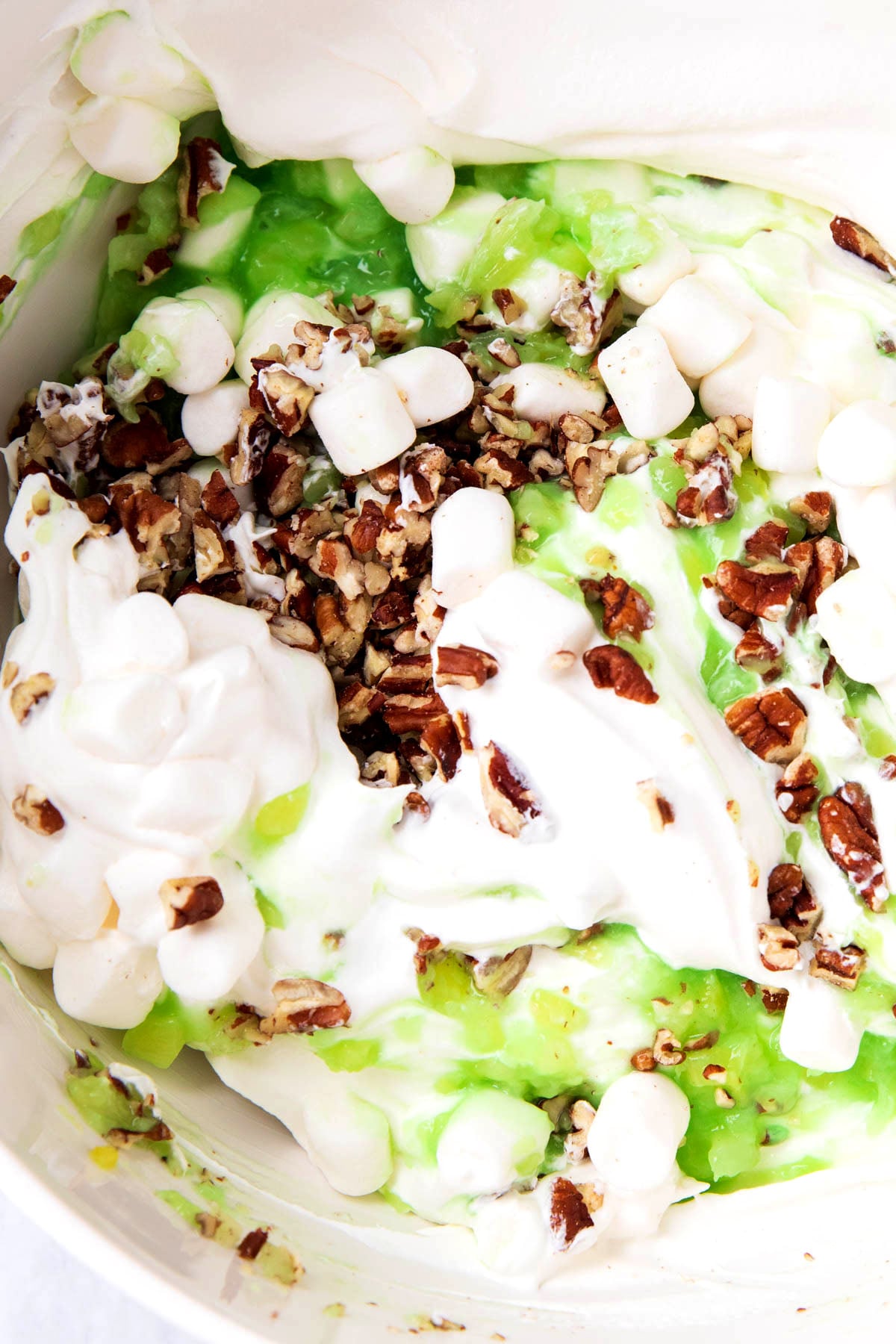Close up of this watergate salad original recipe shows pistachio pudding, marshmallows, and Cool Whip stirred in a mixing bowl.