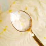 Holding up a spoon of lemon cream cheese frosting to show thick and fluffy texture