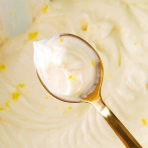 Holding up a spoon of lemon cream cheese frosting to show thick and fluffy texture