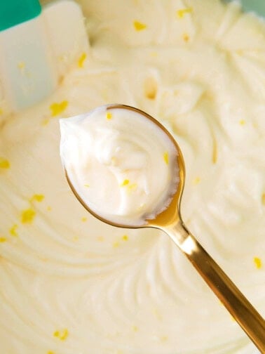 Holding up a spoon of lemon cream cheese frosting to show thick and fluffy texture