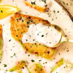 Spooning sauce over creamy garlic and parmesan chicken in a pan with chicken breasts