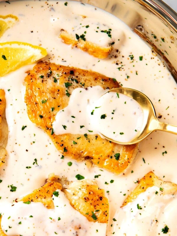 Spooning sauce over creamy garlic and parmesan chicken in a pan with chicken breasts