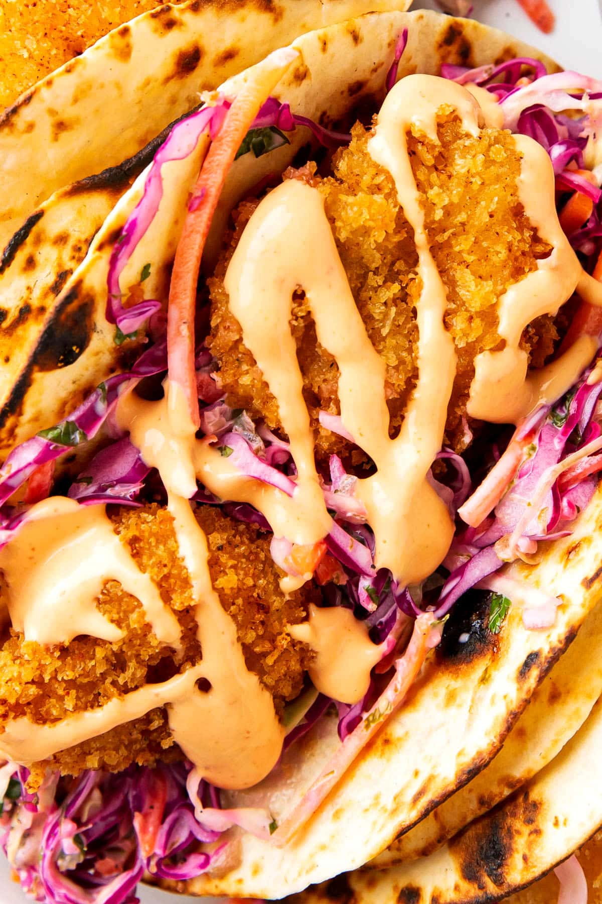 Close up of this fried shrimp tacos recipe shows the crunchy texture of crispy shrimp nestled in sliced red cabbage and tortillas served with sauce and fresh limes.