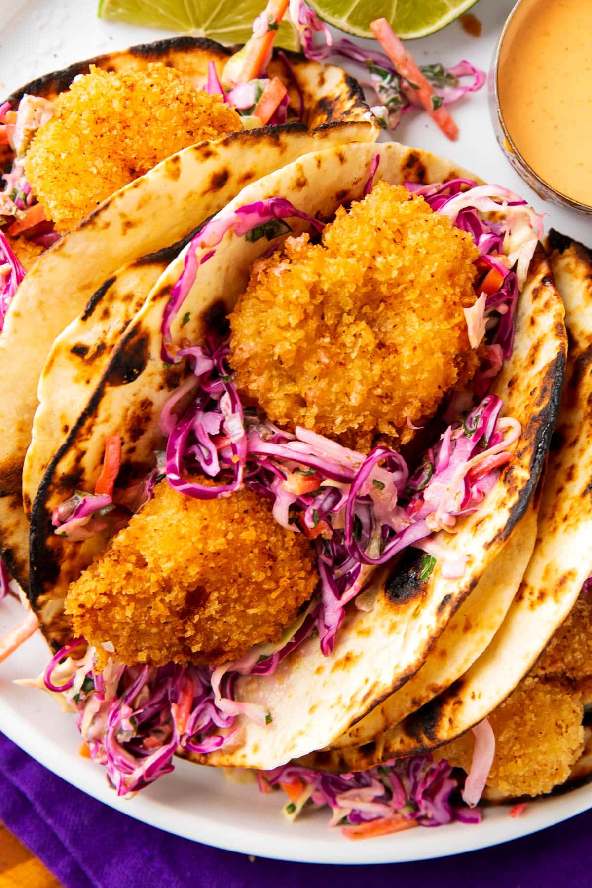 Crispy shrimp tacos recipe served on a plate with lots of golden fried shrimp, cilantro lime slaw, and a creamy sauce for drizzle.