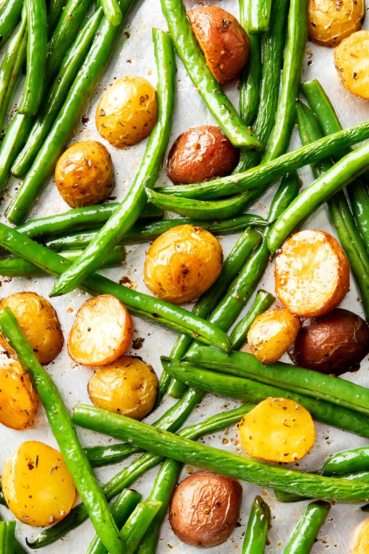 Closeup of this recipe for roasted potatoes and green beans on a baking sheet coated with olive oil and seasonings.