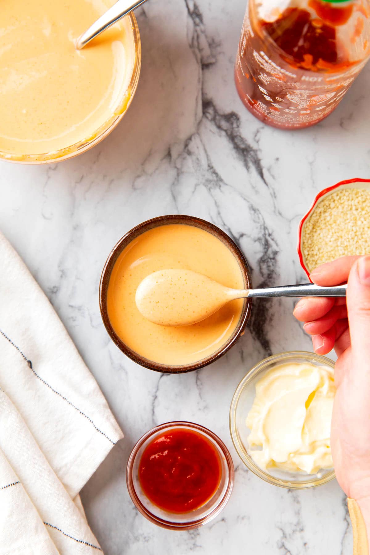 Someone spooning sriracha with mayo in a bowl to be used in a recipe.